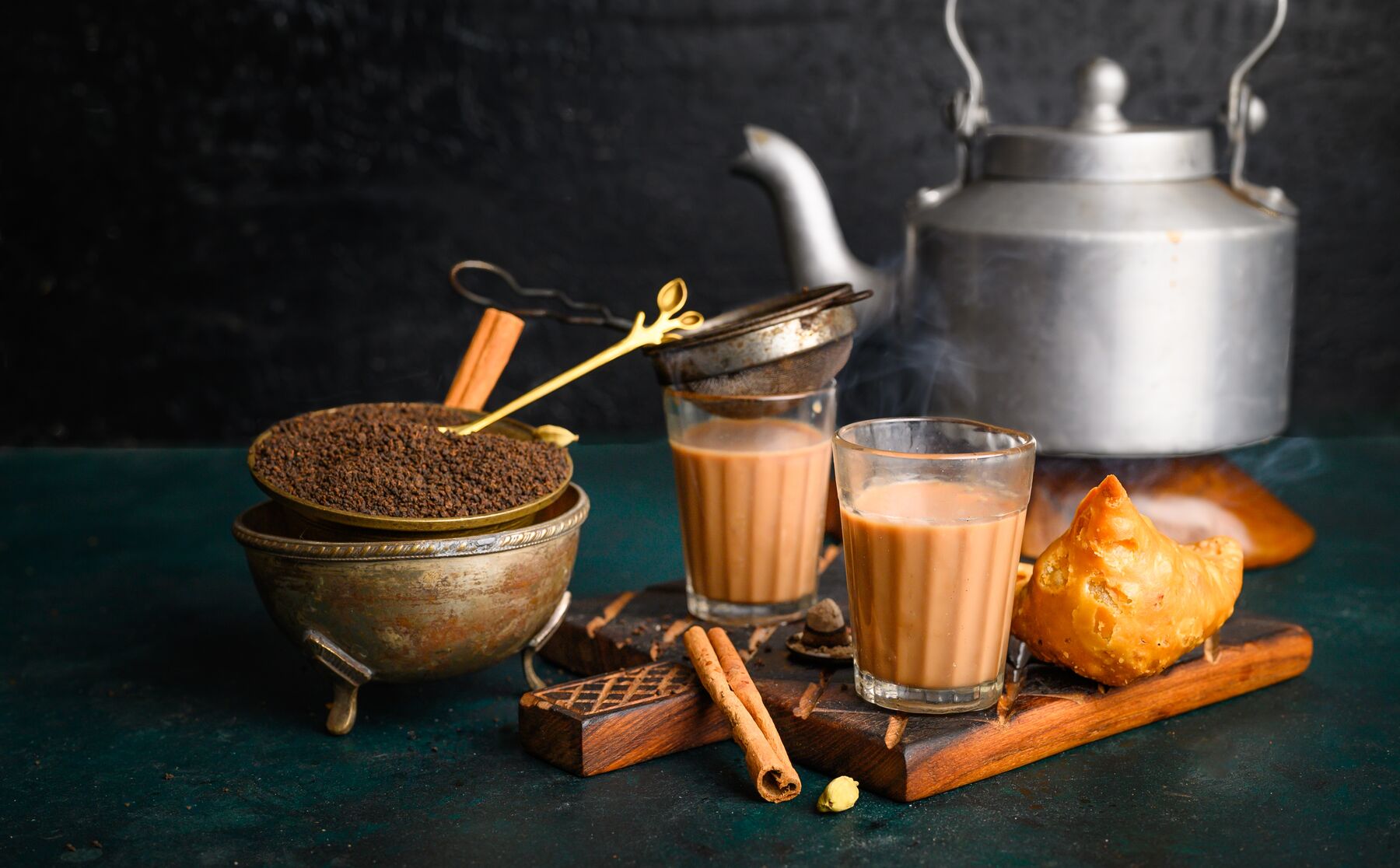 Chai in glass cups beside a kettle and cinnamon